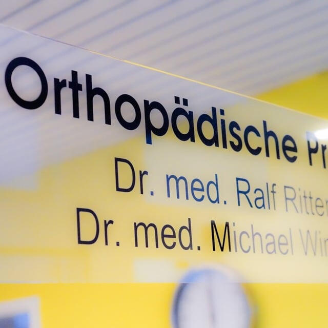 Orthopädische Praxis Dr. Ritter & Kollegen Eingangsbereich der orthopädischen Praxis mit Praxisschild und den Namen der behandelnden Ärzte.